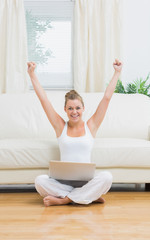 Fototapeta na wymiar Cheerful woman raising hands while using laptop
