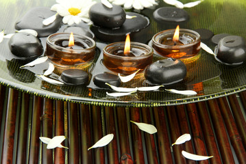 spa stones with flowers and candles in water on plate