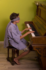 Junge in einem langem Hemd und verbundenen Augen spielt Klavier