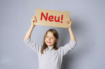 M&auml;dchen h&auml;lt ein Schild mit &bdquo;Neu"-Schriftzug