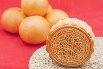 Moon cake on a bamboo mat and some oranges.