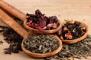 assortment of dry tea in spoons, on wooden background