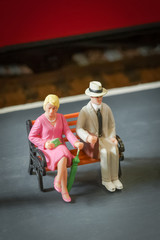 miniature people sitting on a railway station bench