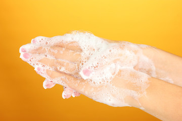 Fototapeta premium Woman's hands in soapsuds, on orange background close-up