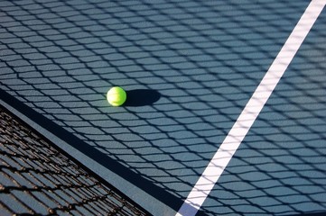 Tennis ball on court in the shadow of the net