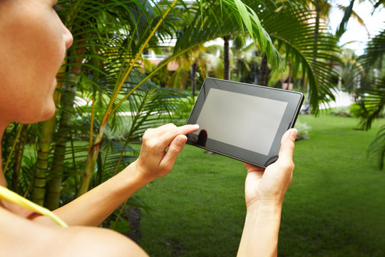 Hands with tablet computer in tropical garden.