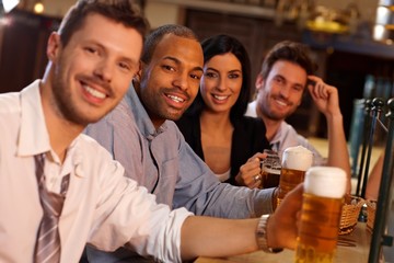Happy young people sitting in pub, drinking beer