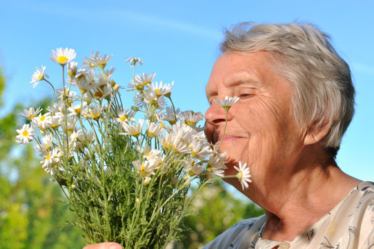 Senior Woman Smelling Flowers On Blue Sky.