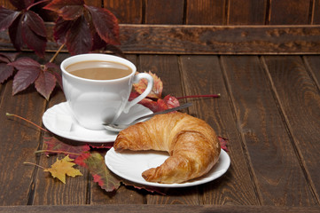 a croissant and a cup of coffeee with milk on a old wooden table