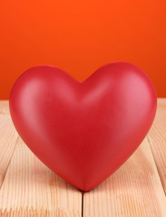 Decorative red heart on wooden table on orange background