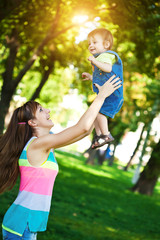 happy mom is throwing  baby in a greenl summer park
