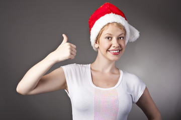 Happy smiley girl in santa hat showing thumbs up
