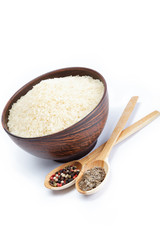 Grains of rice in a bowl and two wooden spoons with spices isola