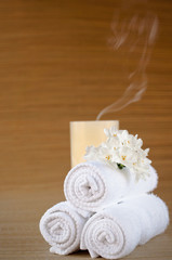 White towels, flower and blown-out candle on brown bamboo mat.