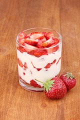 Glass of ripe strawberries with cream on wooden background