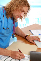 A male doctor filling documents at the desk indoors
