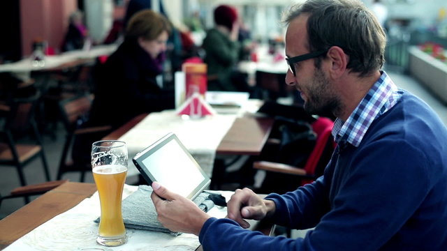Young man with tablet computer drinking beer in the restaurant, 