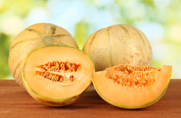 Cut melon on wooden table on green background