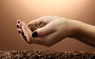 female hands with coffee beans, on brown background