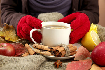 hands holding cup of hot drink and autumn leaves,