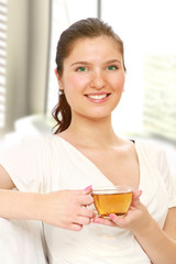 A beautiful woman is drinking tea sitting on sofa indoors