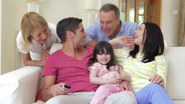 Family Sitting On Sofa Watching TV Being Joined By Grandparents