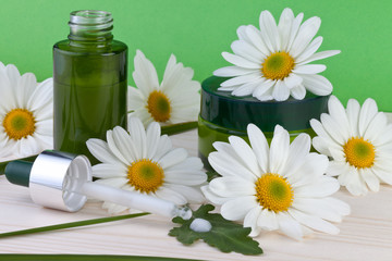 skin care, cream, serum with camomile flowers on green