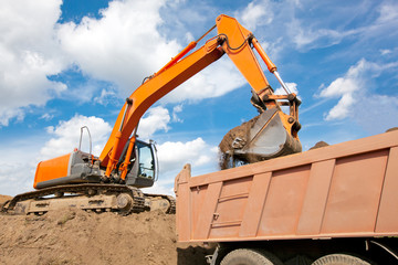 Backhoe loading soil or sand into dump truck body