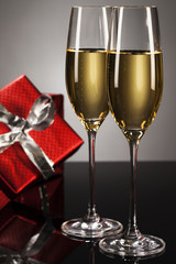 zwei gläser mit champagner vor rotem geschenk auf spiegel