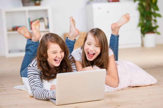 zwei lachende mädchen schauen auf den laptop