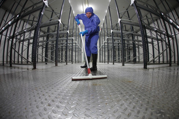 worker in protective  uniform cleaning floor in empty storehouse