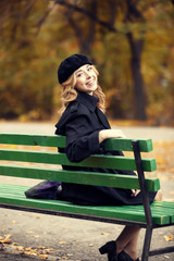 Style redhead girl sitting at bench in autumn park.