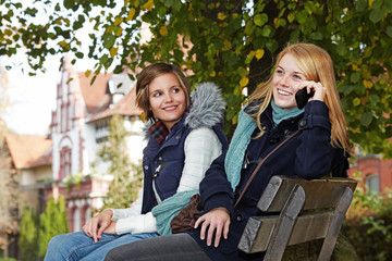 two young women sitting on a park bench