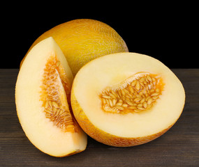 Cut ripe melons on wooden table on black background