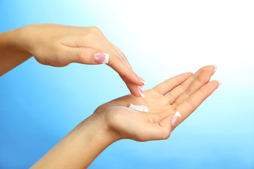 Beautiful woman hands with cream, on blue background