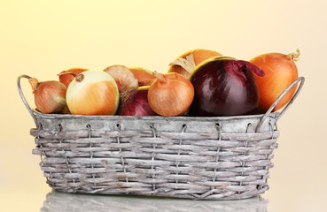 Ripe onions in grey basket on yellow background