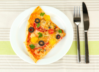 plate with a slice of delicious pizza on tablecloth close-up
