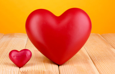 Fototapeta premium Large and small red heart shapes on wooden table with orange background, love and relationship concepts