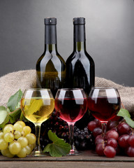 bottles and glasses of wine and grapes on grey background