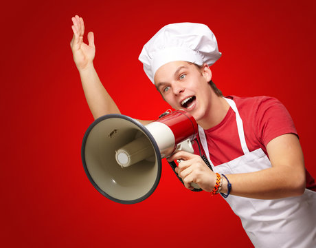 portrait of young cook man shouting with megaphone over red back