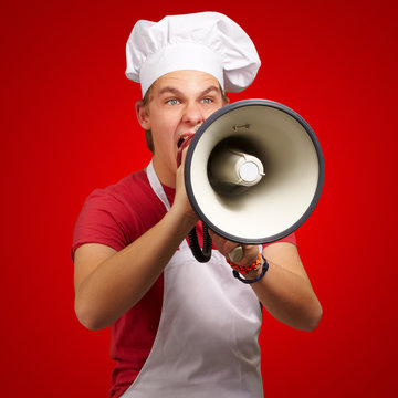 portrait of young cook man screaming with megaphone over red bac