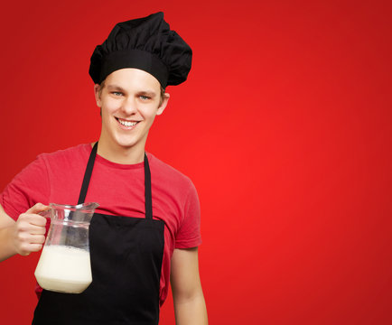portrait of young cook man holding milk jar over red background