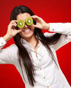portrait of young girl holding kiwi slices in front of her eyes