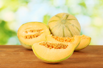Cut melon on wooden table on green background
