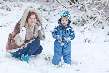 Fototapeta na wymiar Mother and toddler boy having fun with snow on winter day