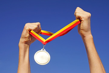 Hands holding gold medal on sky background