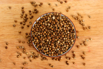 Heap coriander seeds in bowl on wooden background close-up