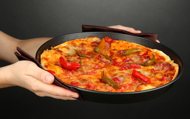 hands holding pepperoni pizza in pan on grey background