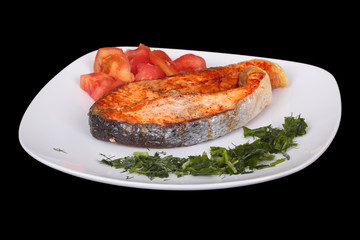 Salmon steak with vegetables on plate. Isolated on black