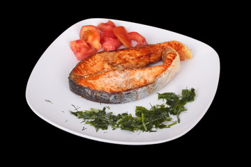 Salmon steak with vegetables on plate. Isolated on black